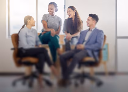 Blurry image of four diverse colleagues smiling and sitting in an office setting.
