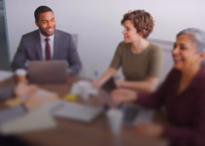 Three business people sitting around a table engaged in discussion in a meeting room.