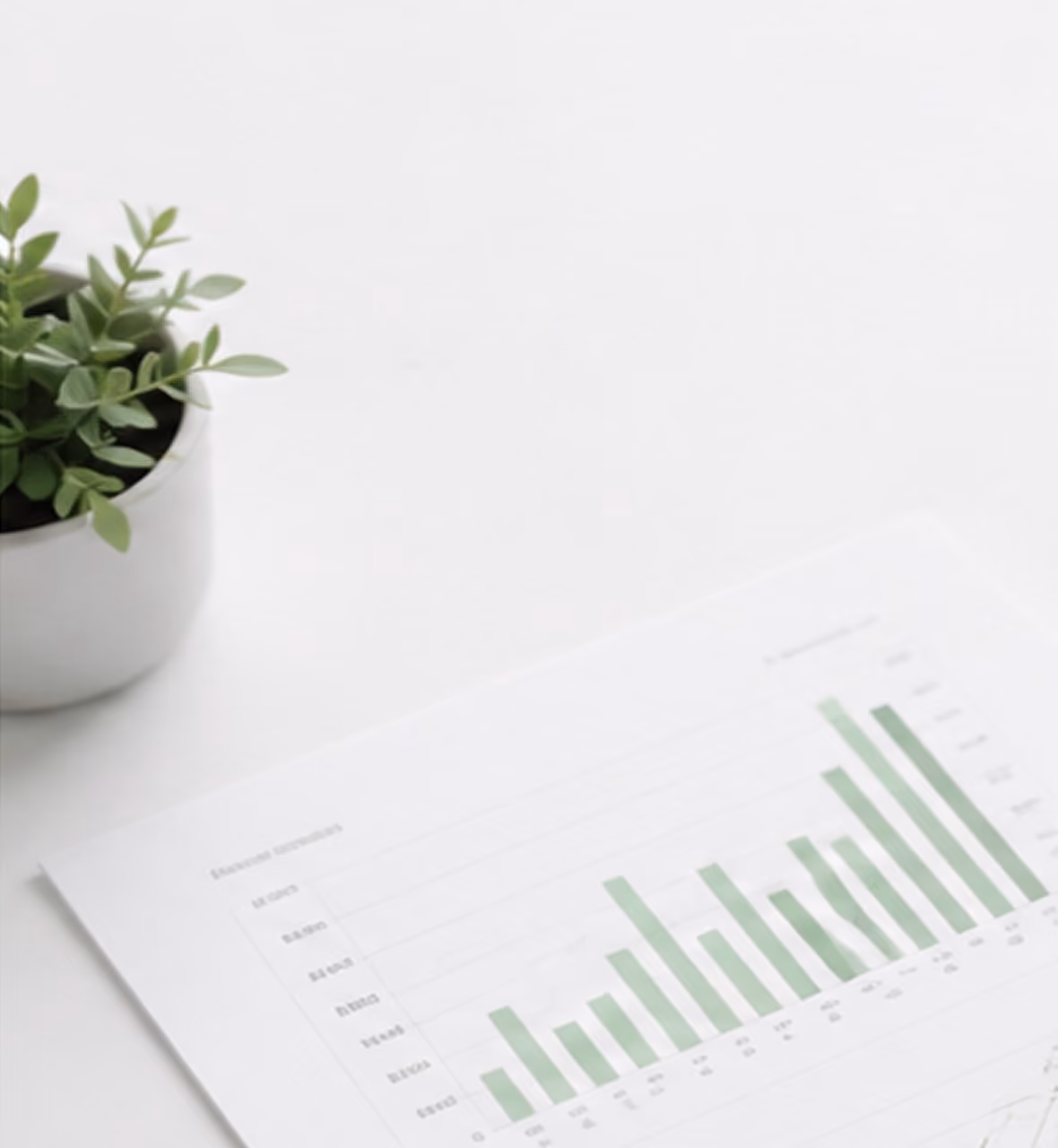 Green potted plant next to a sheet with a green bar chart on a white surface.