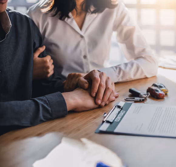 Couple holding hands over a contract on a table with car keys and a toy car nearby.