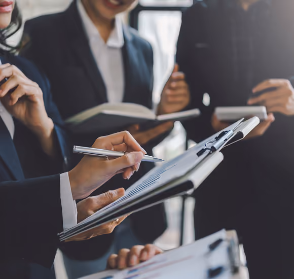 Business professionals in suits holding clipboards and taking notes during a meeting.