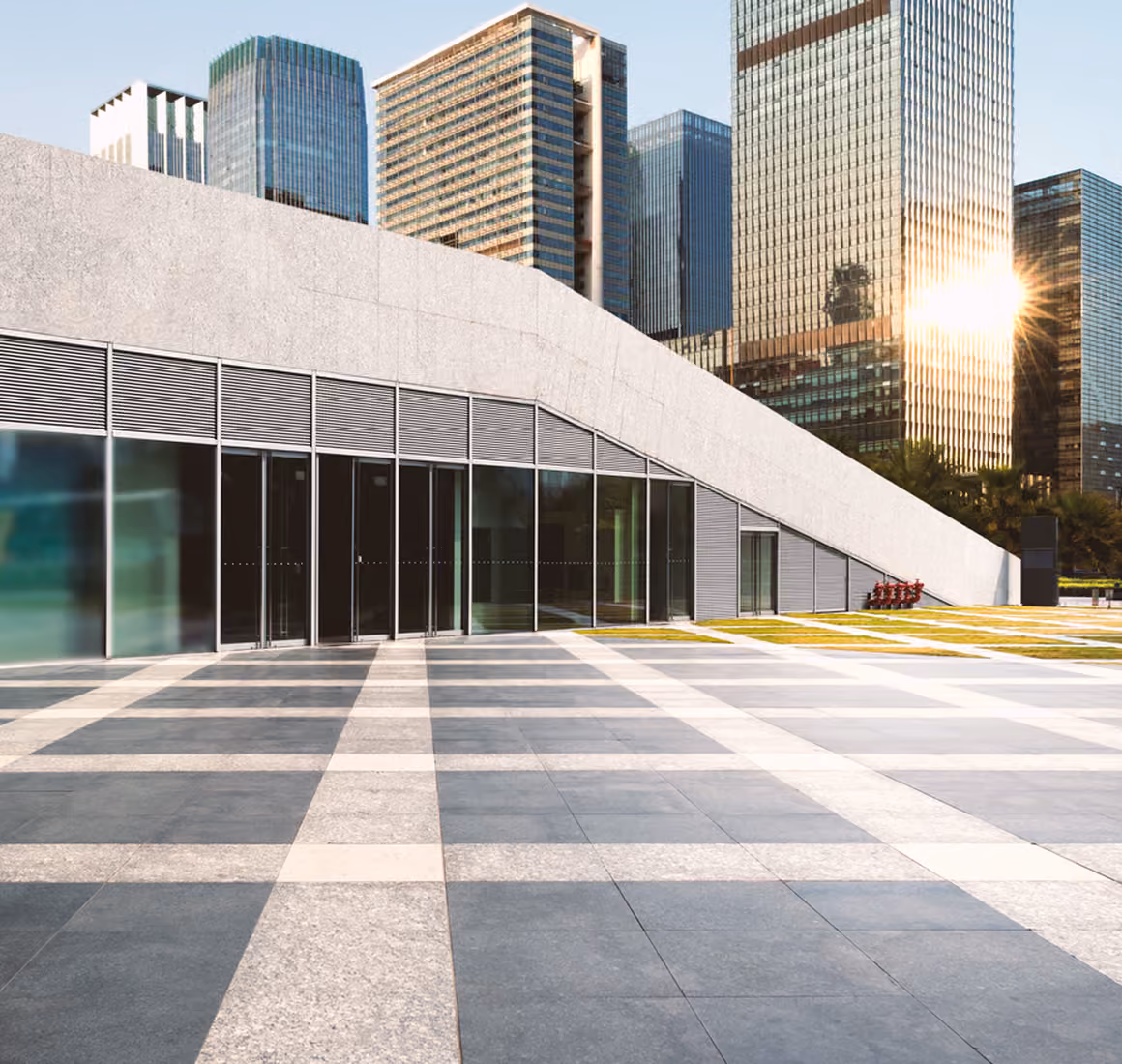 Modern building with large glass doors and stone facade next to skyscrapers reflecting sunlight.